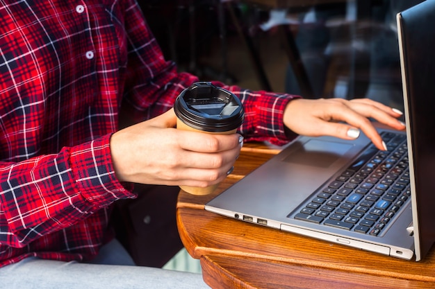 A garota está trabalhando atrás de um laptop em uma mesa em um café ao lado de uma xícara de café