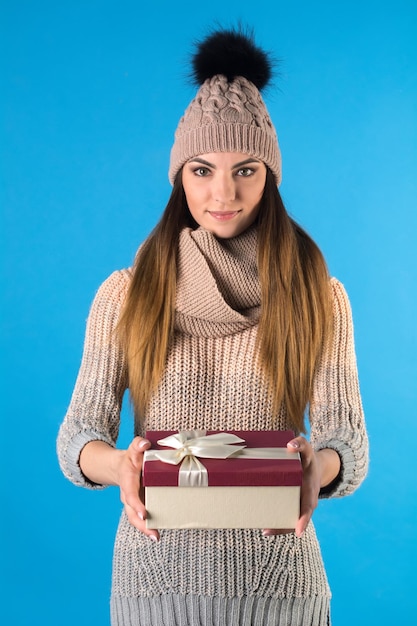 A garota está vestida com um suéter quente de malha e um chapéu com uma caixa de presente