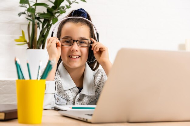 A garota feliz em fones de ouvido com um laptop sentado à mesa em casa