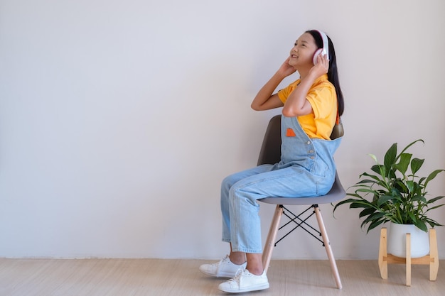 A garota feliz sentada em uma cadeira ouvindo música no quarto mínimo em casa