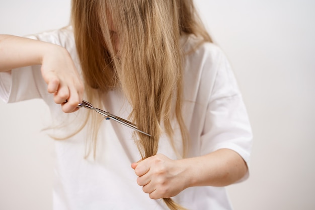 A garota garoto tesoura seus longos cabelos com uma tesoura em um fundo branco. Corte de cabelo elegante para o bebê. Cabeleireiro. brincadeiras infantis. corte de cabelo