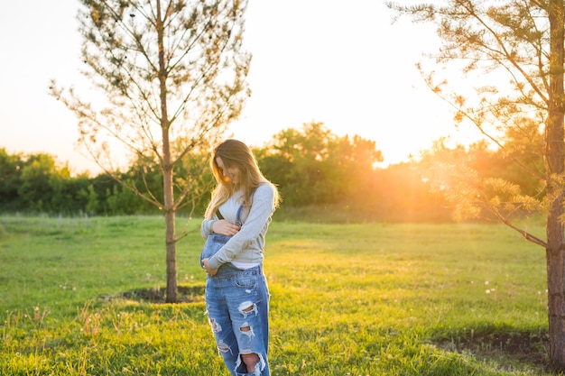 A garota grávida ao ar livre em um pôr do sol