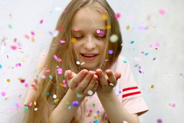 A garota loira feliz soprando o confete em suas mãos