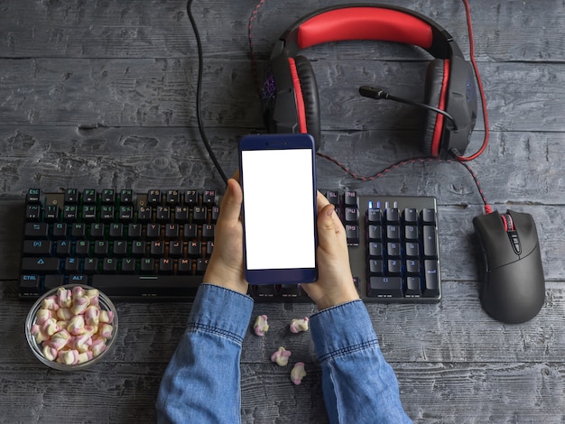 A garota mantém o telefone no fundo de uma área de trabalho com teclado, fone de ouvido e mouse para jogos