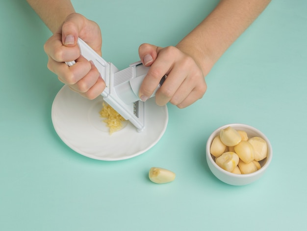 A garota mói alho com um ralador manual. Um tempero popular para a cozinha.