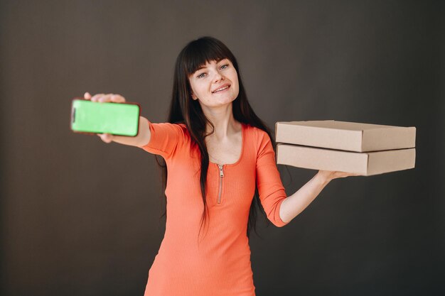 A garota mostra a tela verde do telefone segurando caixas de entrega de comida nas mãos transporte rápido