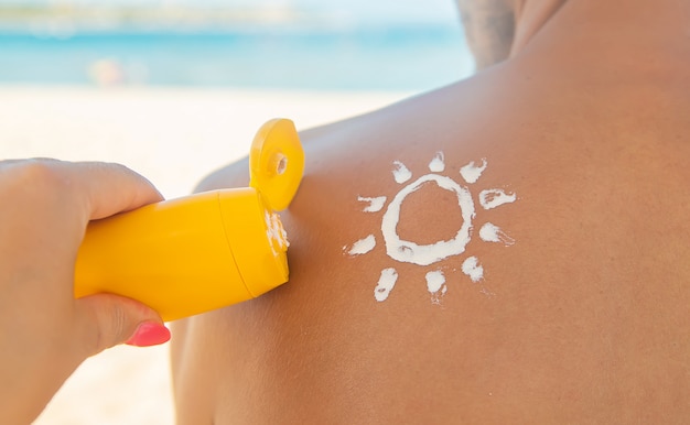 A garota na praia aplica protetor solar na pele de um homem