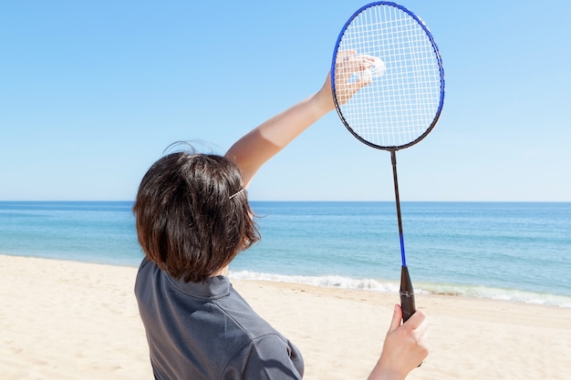 A garota na praia serve jogando badminton. fechar-se.