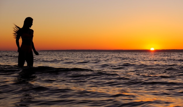 A garota nada no mar, espirra na água ao pôr do sol. Relaxamento e passatempo feliz. Férias de verão.