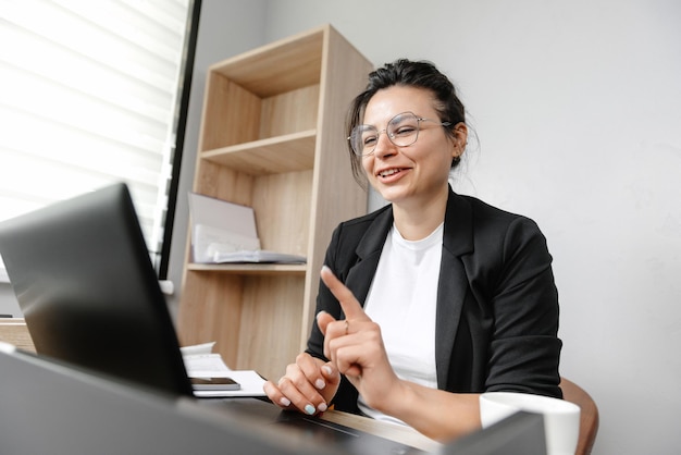 A garota no escritório está realizando uma conferência online e dizendo algo trabalhando em um escritório hyb