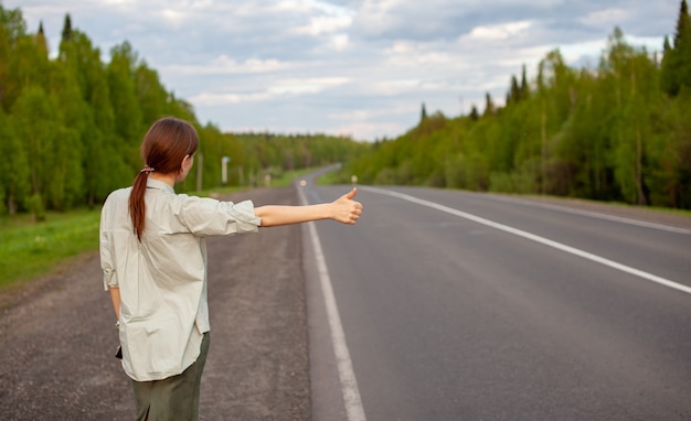 Foto a garota para o carro na rodovia com a mão. mulher elegante na estrada para o carro em uma viagem. uma estrada no meio da floresta.