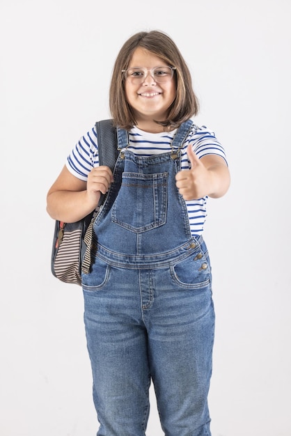 A garota que frequenta a escola usa mochila e mostra o polegar para cima a expressão em um fundo branco isolado