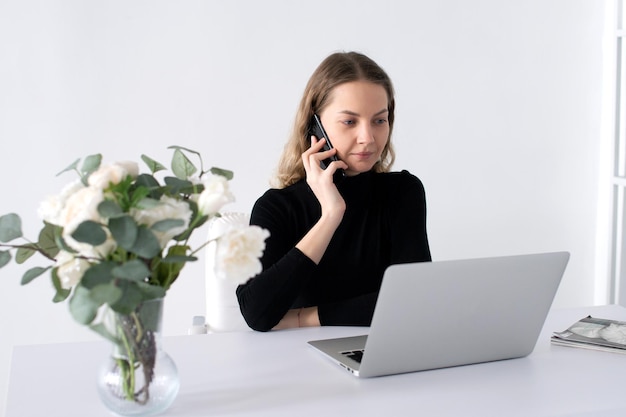 A garota ri e fala ao telefone no escritório ao lado de seu laptop