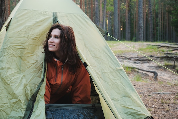 A garota sai da tenda depois de dormir. Viaje para fora da cidade na floresta. Acampamento.