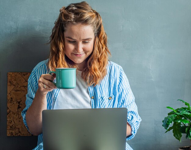 a garota se senta na cama no computador com uma xícara de café chá trabalho freelance em casa remoto