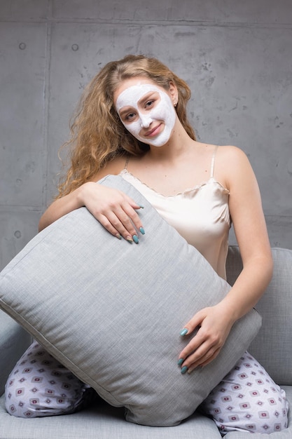 A garota se senta no sofá usando uma máscara cosmética.