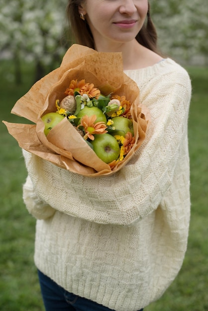 A garota tem um buquê de maçãs e flores nas mãos