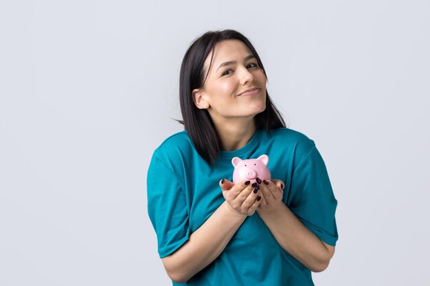 A garota tem um cofrinho rosa e uma moeda nas mãos. O conceito de riqueza e acumulação.