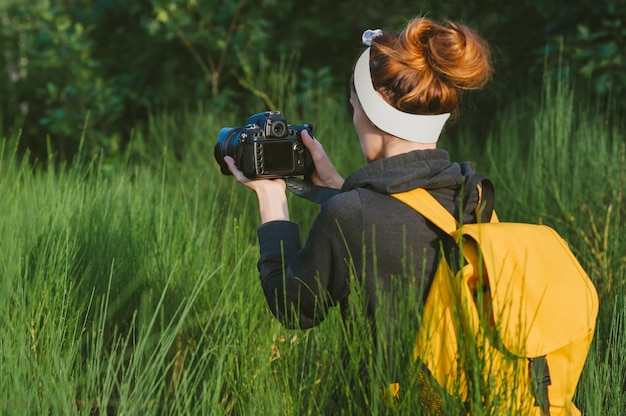 A garota tira fotos com uma câmera SLR na floresta. Contra o pano de fundo de uma bela vegetação.