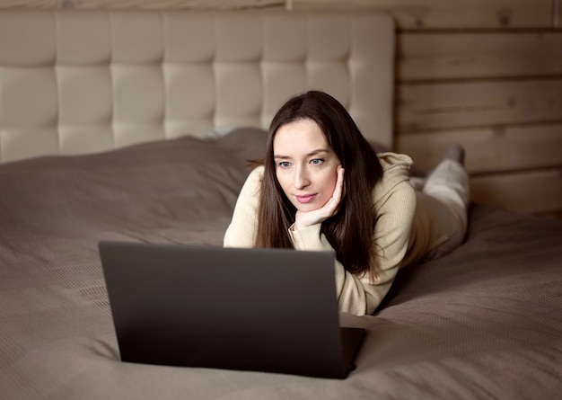 A garota trabalha no computador de casa. um quarto em uma casa de madeira em tons de bege.