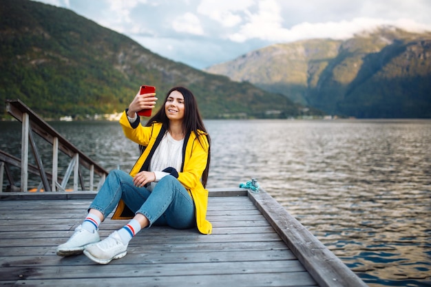 A garota turista tira uma foto no telefone à beira do lago na Noruega Jovem tira selfie