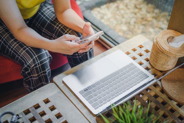 A garota usando smartphone com o computador no café