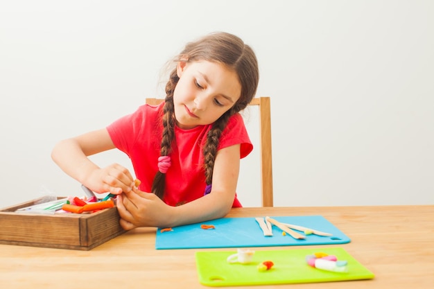 A garotinha está aprendendo a usar argila colorida na mesa