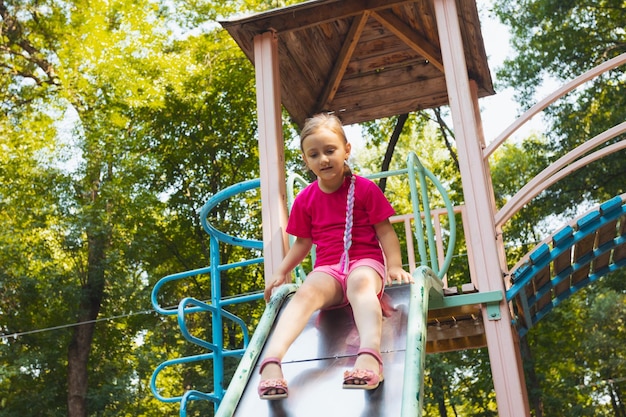 A garotinha está sentada em um escorregador no playground