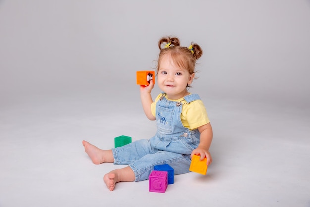 A garotinha está sentada no fundo branco e brincando com cubos coloridos cubos de brinquedo infantil