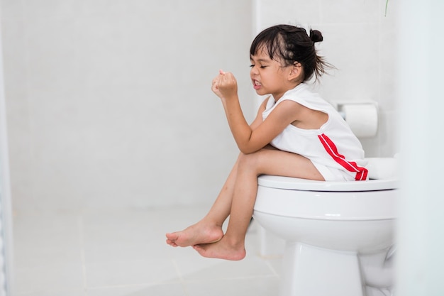 A garotinha está sentada no vaso sanitário sofrendo de constipação ou hemorroida