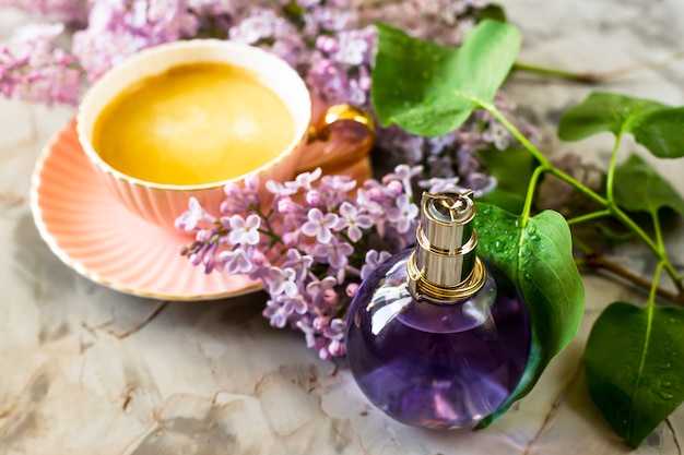 A garrafa violeta de perfume feminino fica ao lado das flores de lilás