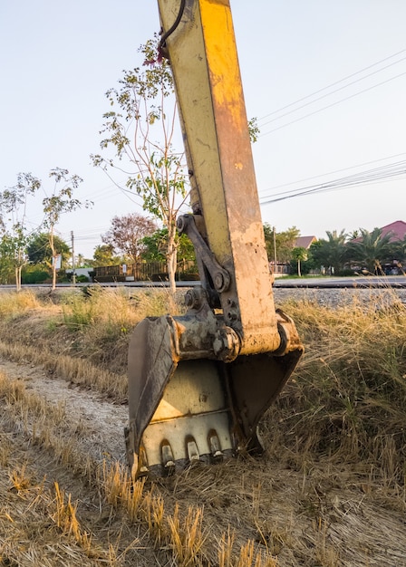 A grande caçamba com a garra afiada da escavadeira está caída no chão no canteiro de obras após o expediente, vista frontal para o fundo.