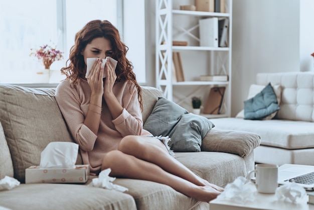 A gripe está me matando! Mulheres jovens doentes assoando o nariz usando lenços faciais enquanto estão sentadas no sofá em casa