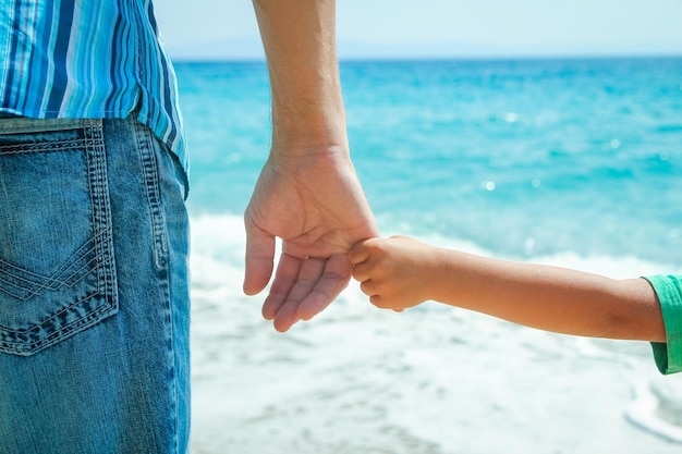 A Hände eines glücklichen Elternteils und Kindes an der Küste auf einer Reise in die Natur