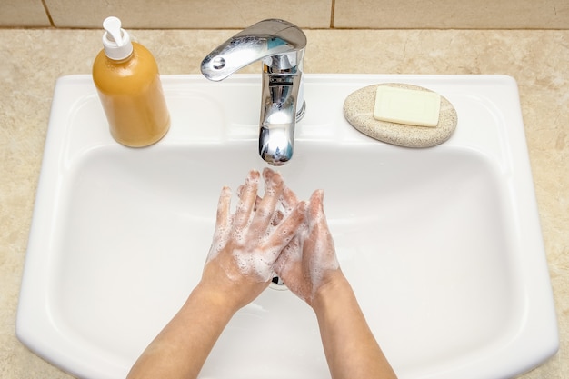 A Händewaschen mit Seife unter dem Wasserhahn mit Wasser