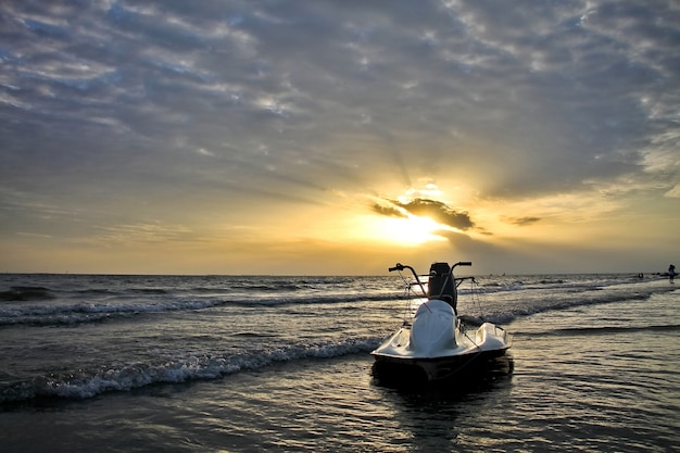 A ideia bonita do por do sol com raio de luz, a nuvem e o jato branco esquiam na praia. Chave baixa. Conceito de natureza e esporte.