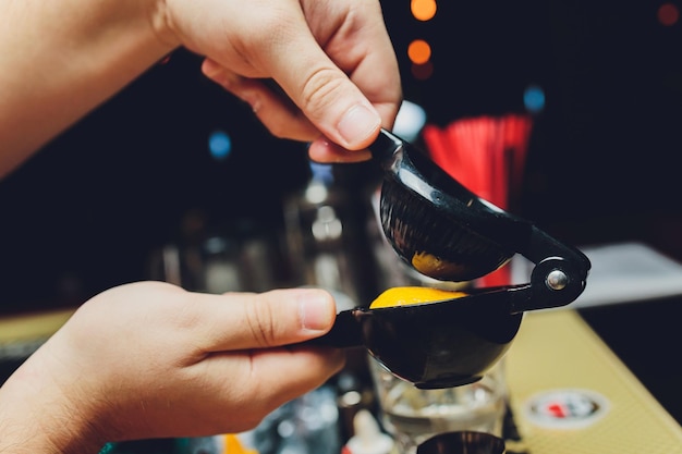 A imagem aproximada das mãos de um barman espreme o suco de limão em uma coqueteleira gelada no balcão do bar