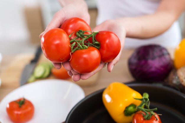 A imagem da opinião superior do close-up das mãos fêmeas que mostram tomates vermelhos suculentos frescos sobre a mesa de cozinha, apronta-se para cozinhar em casa.