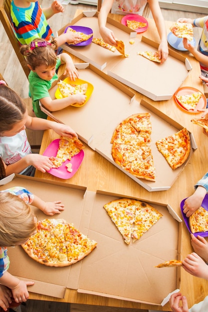 A imagem da vista superior das crianças pega fatias de pizza da caixa na cozinha. festa infantil em casa