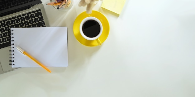 A imagem da vista superior de uma xícara de café está sobre uma mesa branca, cercada por equipamentos de escritório.