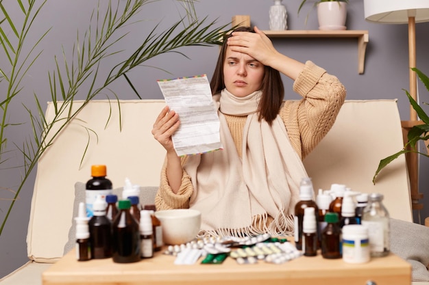 A imagem de uma mulher caucasiana doente e insalubre lendo instruções antes de tomar medicação sofrendo de dor de cabeça terrível tocou sua testa com alta temperatura