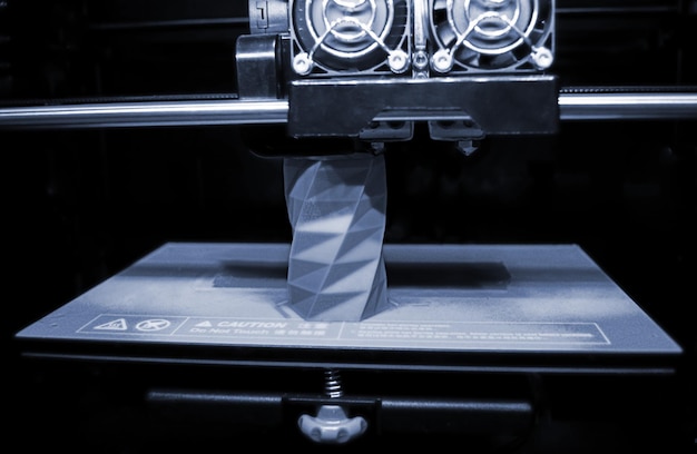 A impressora 3D funciona e cria um objeto a partir do close-up de plástico derretido a quente. A impressora 3d tridimensional automática realiza modelagem de cores cinza azul de plástico em laboratório.