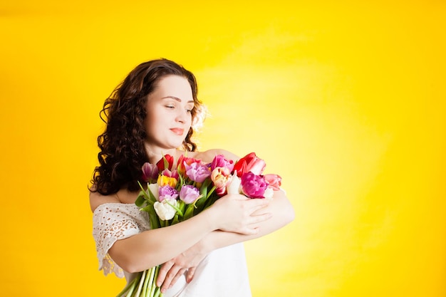 A incrível garota de vestido branco com lindas tulipas em um fundo amarelo