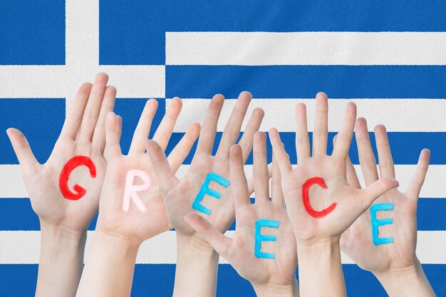 A inscrição Grécia nas mãos das crianças contra a superfície de uma bandeira ondulante da Grécia