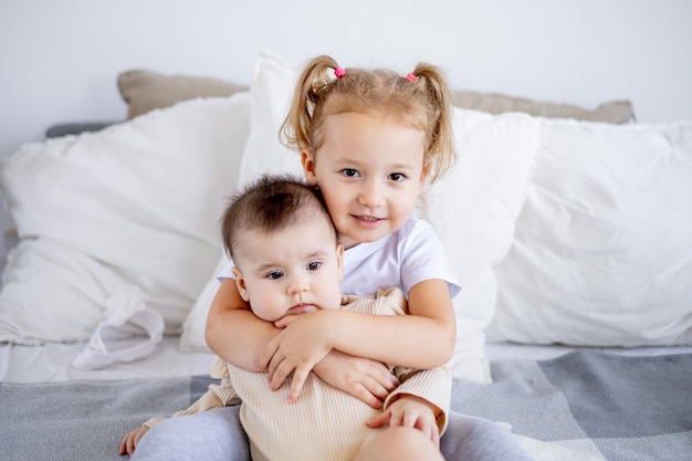 A irmã mais velha segura e abraça o bebê em casa na cama o amor e a amizade das irmãs da família