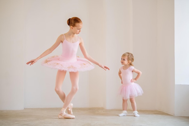 Foto a irmã mais velha, uma bailarina de tutu rosa e sapatilhas de ponta, mostra ao bebê como praticar na barra