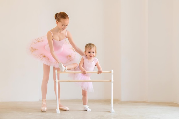 A irmã mais velha, uma bailarina de tutu rosa e sapatilhas de ponta, mostra ao bebê como praticar na barra