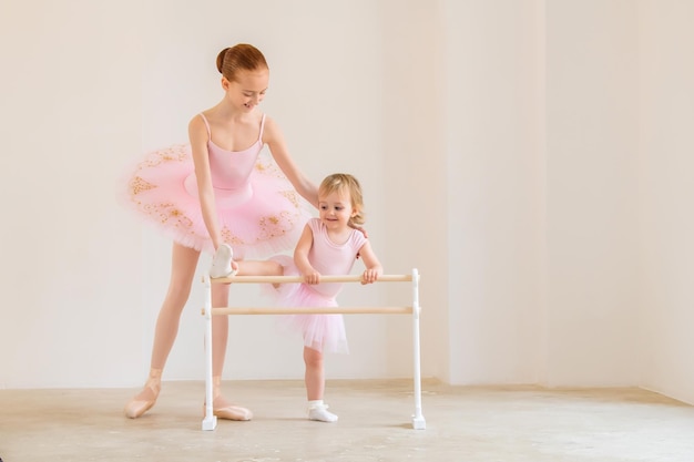 A irmã mais velha, uma bailarina de tutu rosa e sapatilhas de ponta, mostra ao bebê como praticar na barra