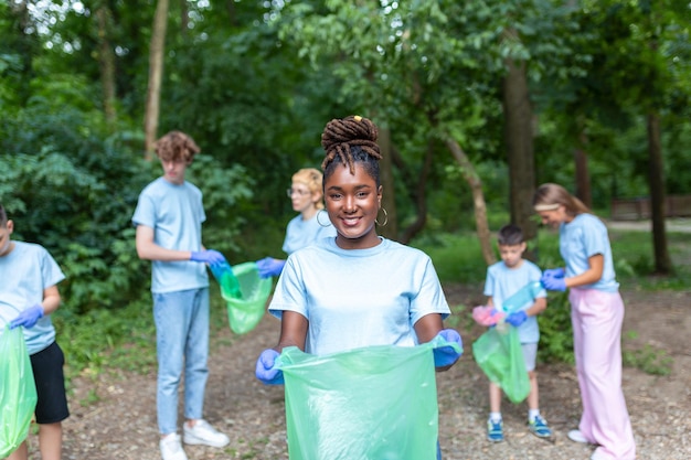 A jovem adulta, que faz parte de um grupo diversificado de voluntários, leva tempo para sorrir para a câmera, segurando um saco de lixo e olhando para a câmara.