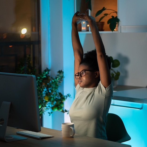 A jovem africana cansada faz uma pausa no trabalho no computador em casa faz exercícios e alongamentos